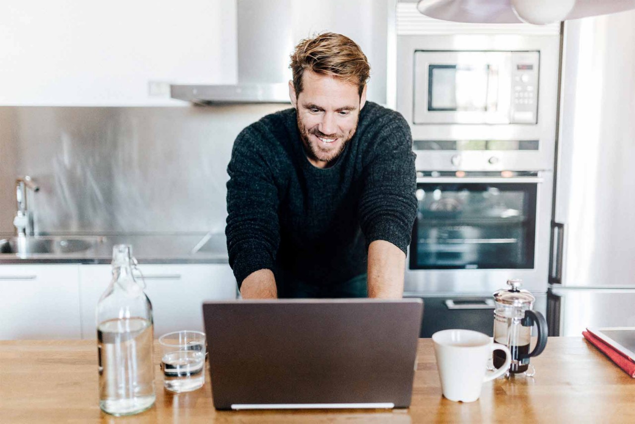 Portrait of smiling man standing in kitchen using laptop; Gettyimages: 882156092